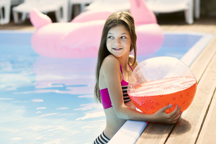 Girl in a striped swimsuit holding a red beach ball by the pool, relating to weird calls first responders faced online.