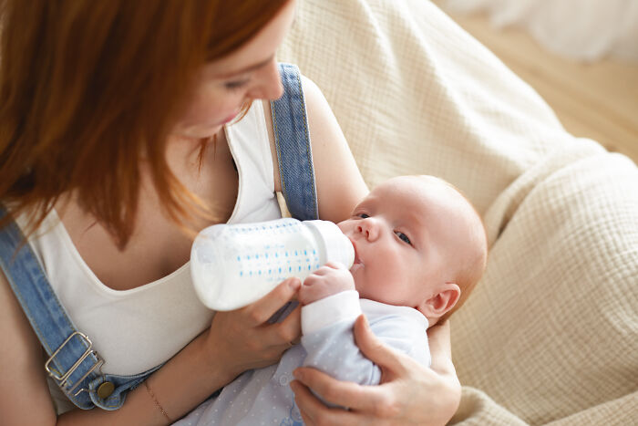 Woman feeding a baby with a bottle while sitting on a couch, illustrating unusual scenes first responders encounter.