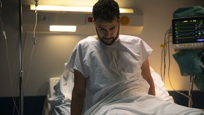 Man in hospital gown sitting on bed, connected to medical monitors, depicting first responders' weird calls scenario.
