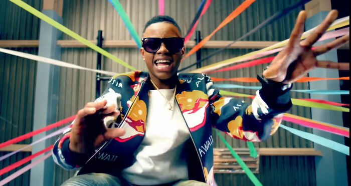 Young man wearing sunglasses and a colorful jacket reaching out amid vibrant ribbon-like decorations, illustrating weird calls first responders face.