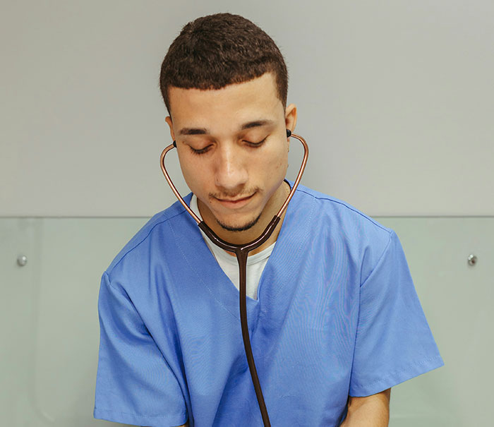 Young medical professional in blue scrubs using a stethoscope, focused on patient care and condition assessment.
