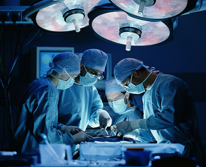 Medical professionals performing surgery in a dimly lit operating room focused on a complex patient condition.
