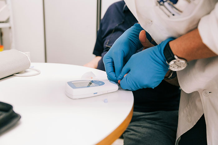 Medical professional wearing blue gloves conducting a blood sugar test with a glucose meter on a white table.