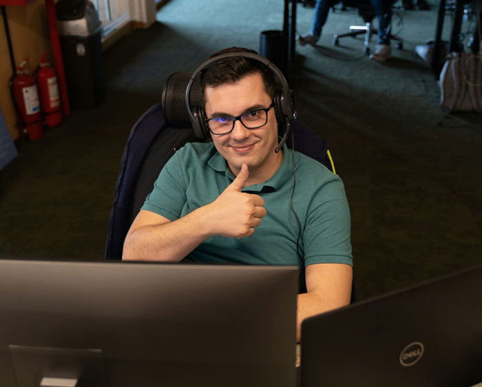 IT professional wearing headset and glasses, sitting at desk with multiple monitors, giving thumbs up in office setting - 11