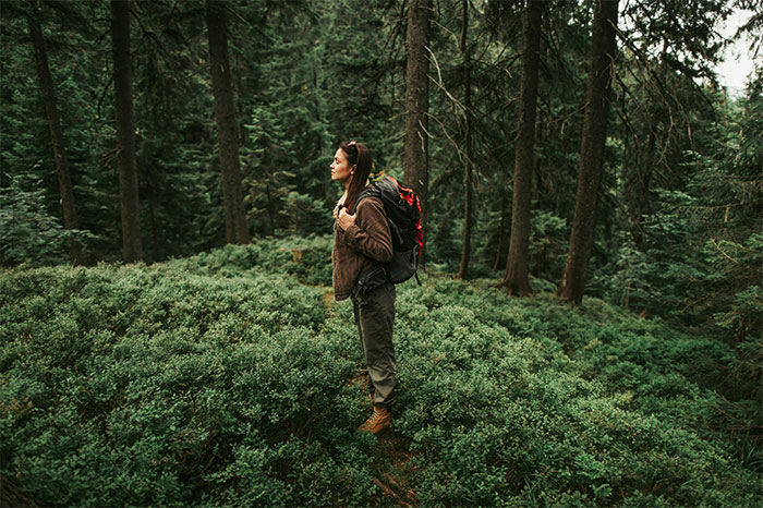 Woman with backpack standing in dense forest surrounded by greenery, evoking creepy and terrifying facts atmosphere