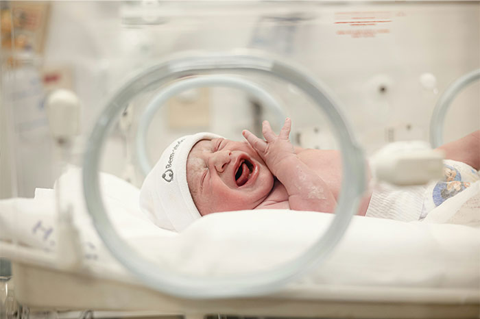 Newborn baby crying inside a hospital incubator, illustrating creepy and terrifying facts about early life struggles.