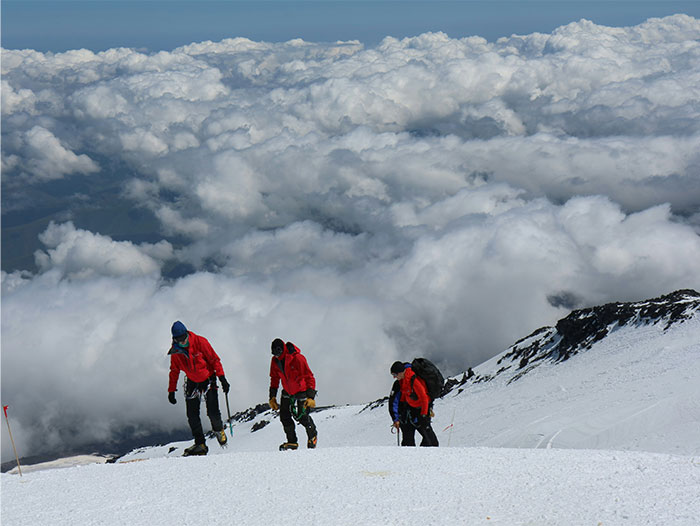 Three climbers in red jackets ascending a snowy mountain slope under a cloudy sky, evoking creepy and terrifying facts.