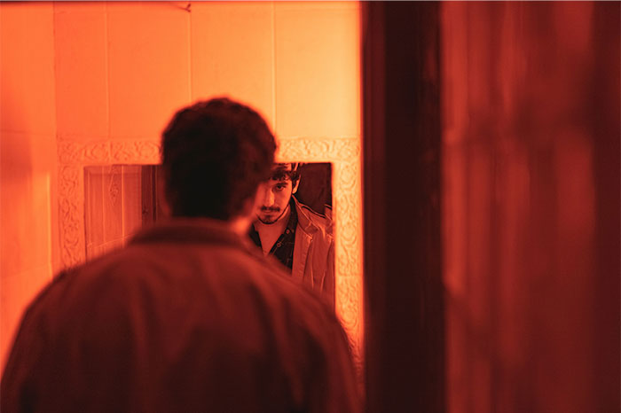 Man with an intense expression looking at himself in a mirror under creepy and terrifying dim orange lighting.