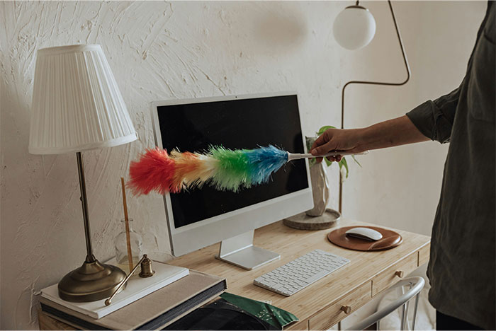 Person using a colorful duster to clean a desk and computer in a room with a lamp and minimal decor, creepy facts concept.