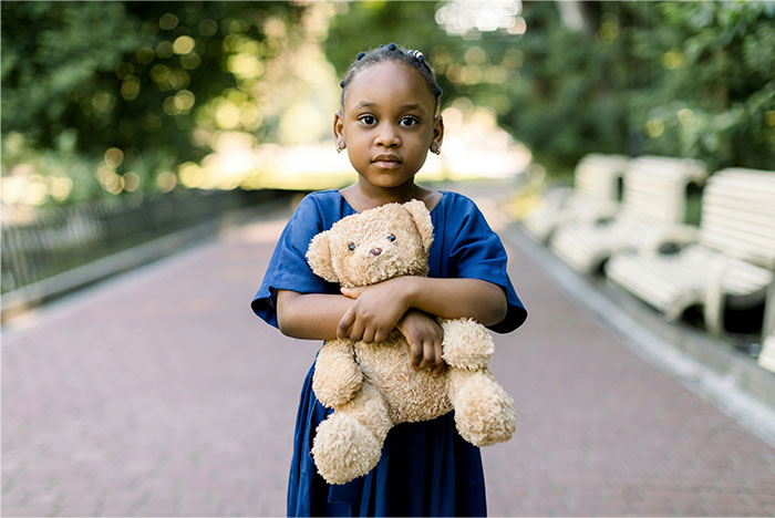 Young girl standing on a park pathway holding a teddy bear, evoking a sense of creepy and terrifying facts atmosphere.