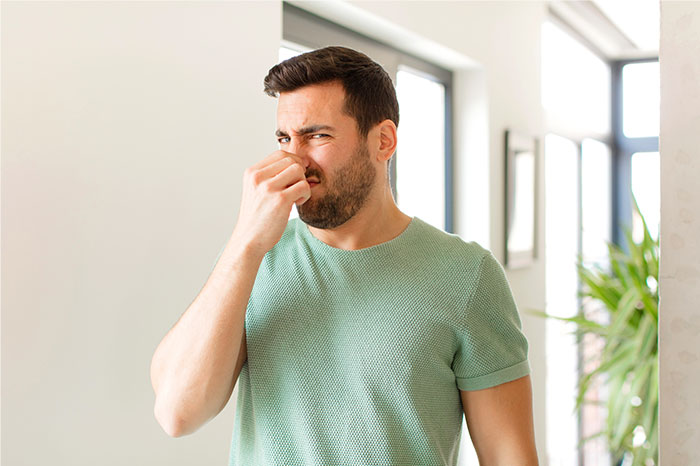 Man in green shirt indoors holding nose with disgusted expression illustrating creepy and terrifying facts.