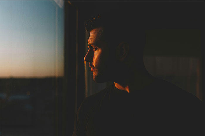Man staring out window at sunset with a pensive expression reflecting on creepy and terrifying facts.