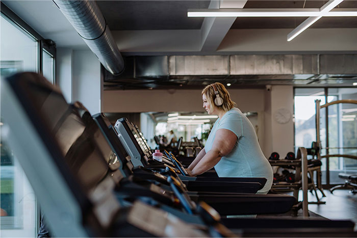 Woman wearing headphones using treadmill in a gym, illustrating creepy and terrifying facts about personal health.