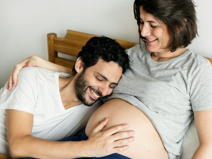 Smiling couple bonding over pregnancy, highlighting emotional and physical experiences women face after birth.