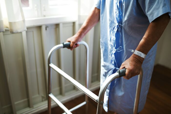Patient using a walker in a hospital gown with identification wristband, illustrating impostor patients needing common sense and less meds.