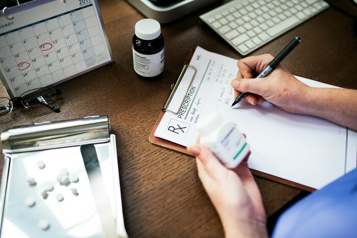 Person writing prescription with antidepressant medication bottle on desk showing withdrawal dangers concept