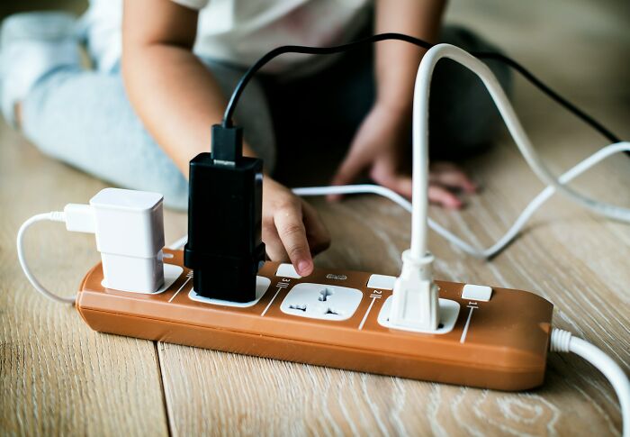 Child's hand reaching towards multiple plugged-in adapters on a power strip illustrating mysterious body quirks concept.