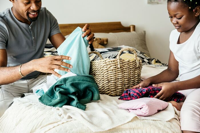 Man and girl folding laundry together on bed, illustrating qualities that make a man instantly unattractive to women.