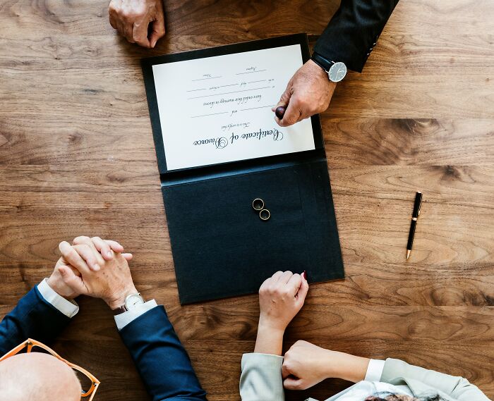 Overhead view of married couple with wedding certificate and rings on wooden table during discussion.