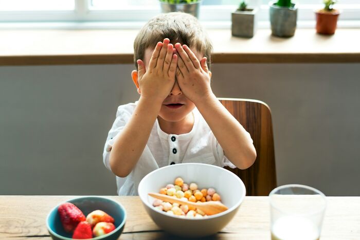 Young boy covering his face at the breakfast table with cereal and fruit, illustrating moments of arrogance and regret.