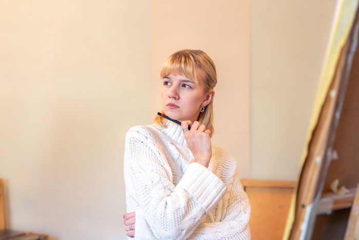Young woman in a white sweater holding a pen, looking thoughtful about dad and stepmom family issues. - 1