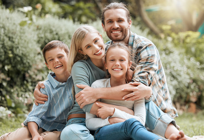 Smiling family outdoors with dad, daughter, stepmom, and son embracing, highlighting blended family dynamics. - 5