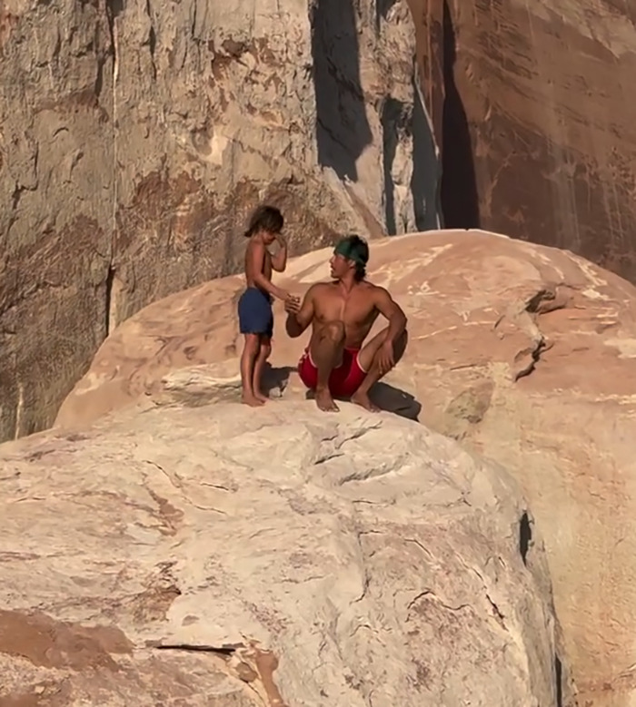 Man and young boy on rocky cliff edge during an outdoor moment related to dad teaching son to face fears controversy. - 1