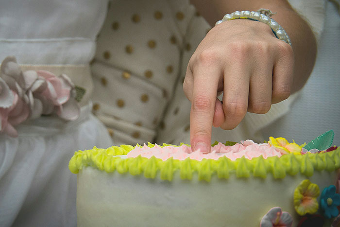 Child touching pink frosting on birthday cake with green and yellow decorations at a party with an unwanted guest present Child touching pink frosting on birthday cake with green and yellow decorations at a party with an unwanted guest present