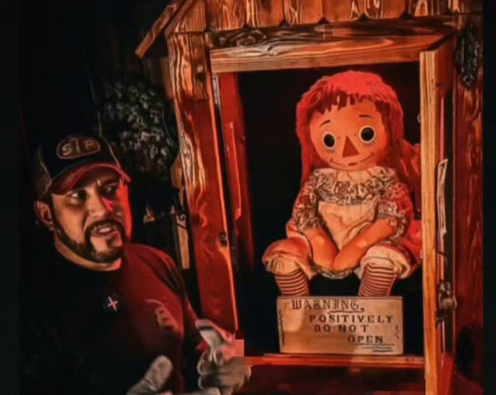 Paranormal investigator standing near a possessed Annabelle doll in a wooden display case with warning sign.