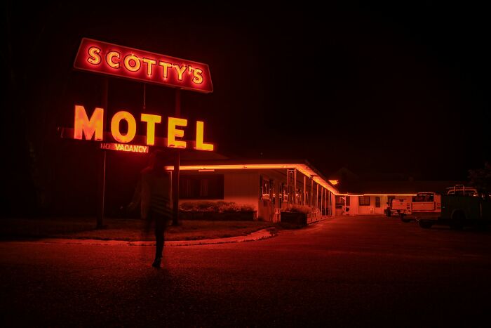 A person walking alone at night near a glowing motel sign, illustrating stories of people who ran away from home. - 19