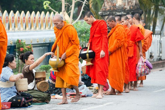 Buddhist monks in orange robes receiving alms from seated women, illustrating common religious myths about faith and tradition.