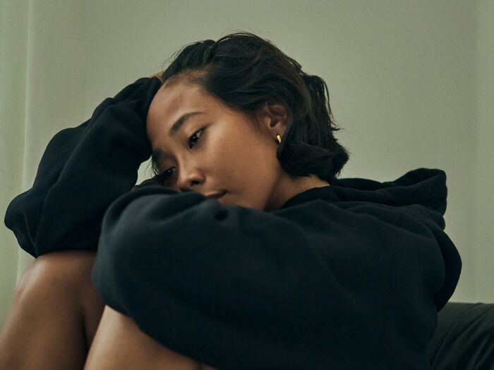 Young woman in black hoodie sitting with knees drawn up, appearing contemplative, illustrating antidepressant withdrawal effects.