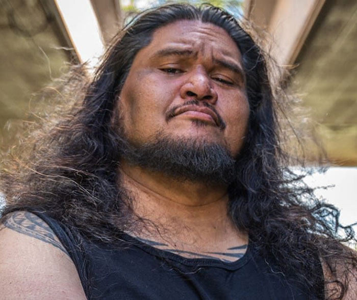 Man with long hair and beard wearing a black tank top, representing stars we've lost this year in July.