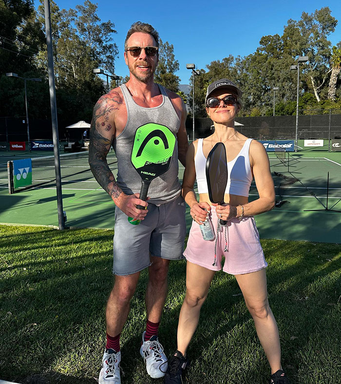 Dax Shepard and Kristen Bell posing on a pickleball court holding paddles during a sunny outdoor game. - 7