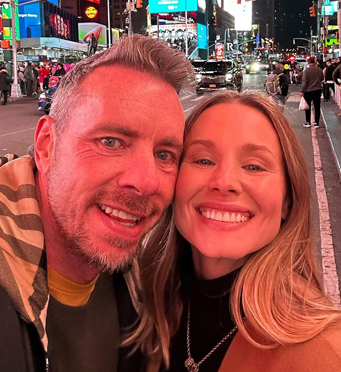 Dax Shepard and Kristen Bell smiling together in a nighttime city setting with suns out buns out vibe.