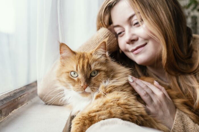 Young woman peacefully resting near a window with her orange cat, illustrating deaf people reveal surprisingly silent things.