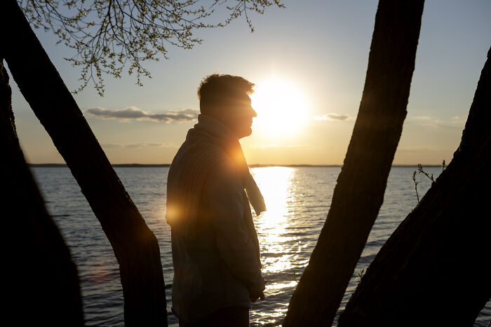 Silhouette of a person standing by water at sunset, reflecting on silent things assumed to be noisy by deaf people.
