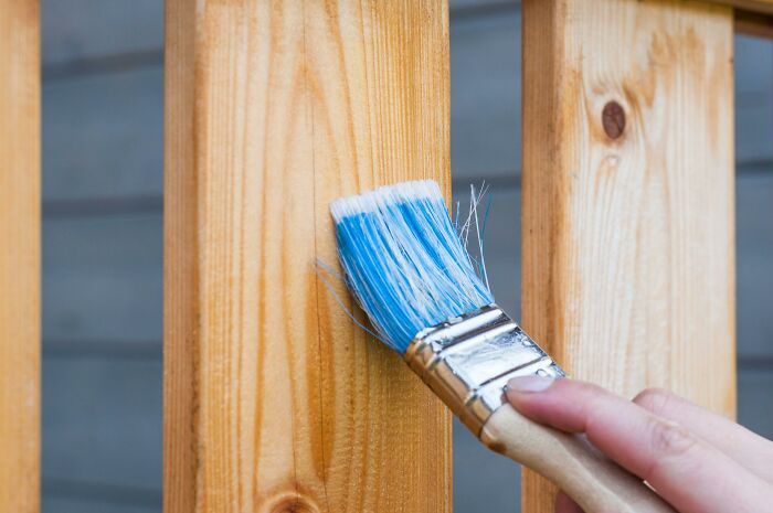 Hand painting wooden surface with blue paintbrush, illustrating silent things deaf people reveal as surprisingly noise-free.