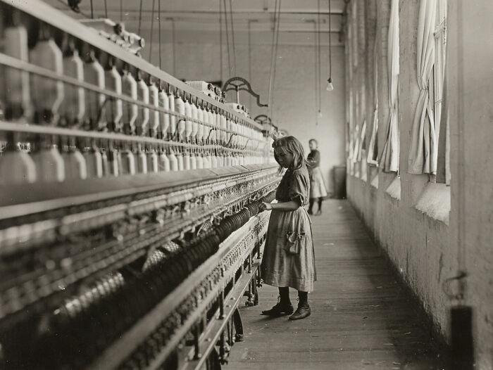 Young girl working in a textile factory during the Industrial Revolution captured in a somber photo from history.