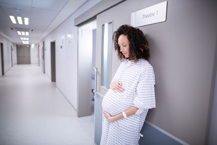 Pregnant woman in delivery room hallway, preparing for birth, relating to delivery room baby DNA testing process. - 1