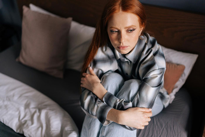 Sad woman sitting on bed hugging knees, upset about ruined $25 yard fabric damaged by guest’s kids. - 14