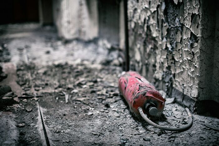 Old, abandoned hallway with peeling paint and a damaged fire extinguisher symbolizing awful roommates’ neglect and mess.