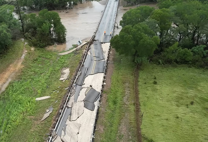 Damaged bridge over floodwaters with two workers inspecting the site, highlighting impact of young flood victim's final message.