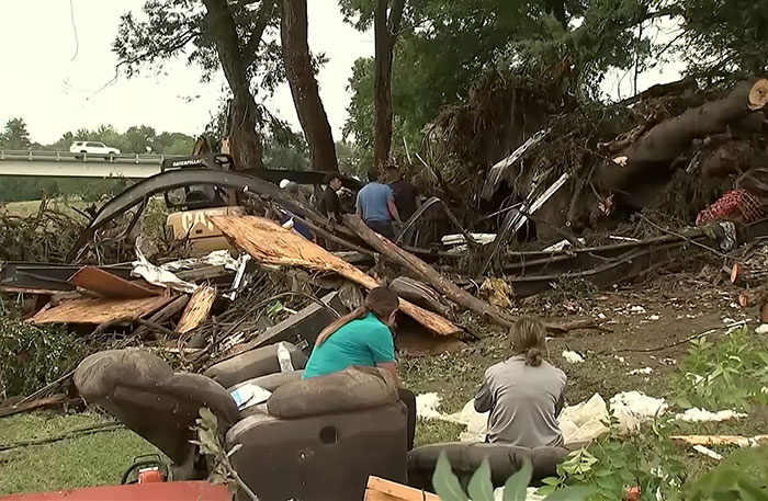 People sitting near debris and wreckage in flood aftermath, reflecting on the fear experienced by the young flood victim.