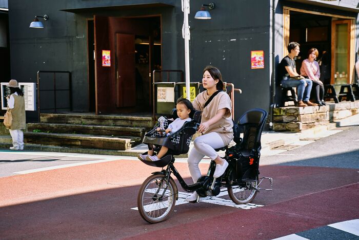 Woman riding bike with child in seat on urban street, representing struggles of married people wishing to be single.