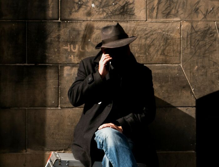 Shadowed person in a hat and coat smoking a cigarette against a graffiti-covered brick wall, evoking school incident mystery. - 30