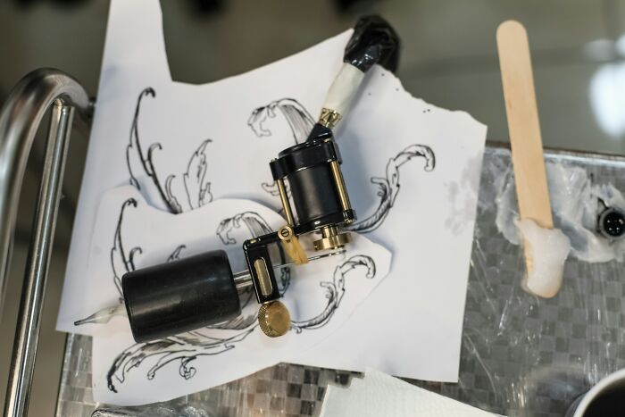 Tattoo machine resting on paper with artistic designs, illustrating ingenious inventions repurposed creatively over the years.