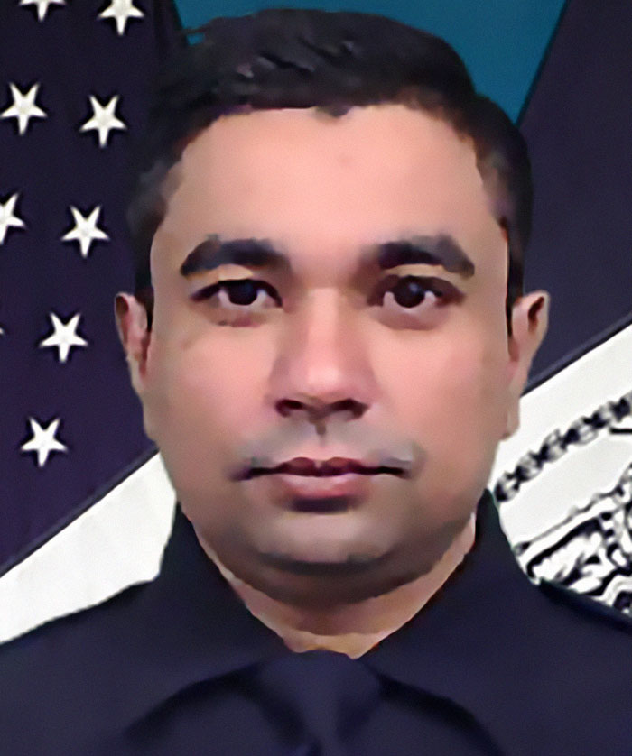 NYPD cop in uniform with American flag background, honored for protecting others and fatally shot in line of duty.