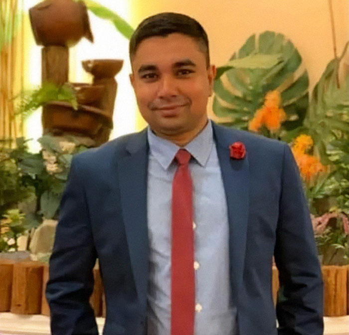 NYPD cop in a suit with a red tie, smiling in a decorated indoor setting, honored for protecting others.