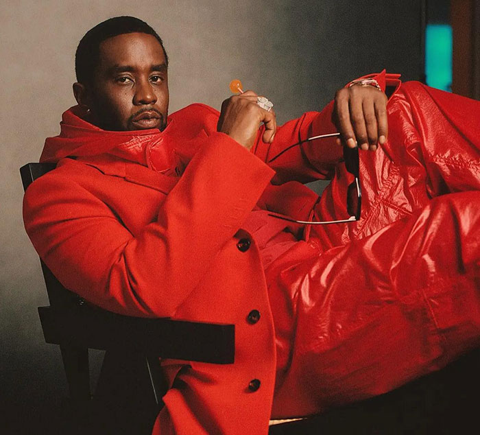 Diddy wearing a red outfit, seated with a serious expression during his trial as the judge receives a surprise note from the jury.